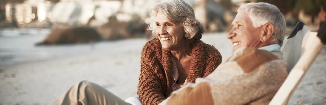 Retired couple laughs while lounging on a beach.